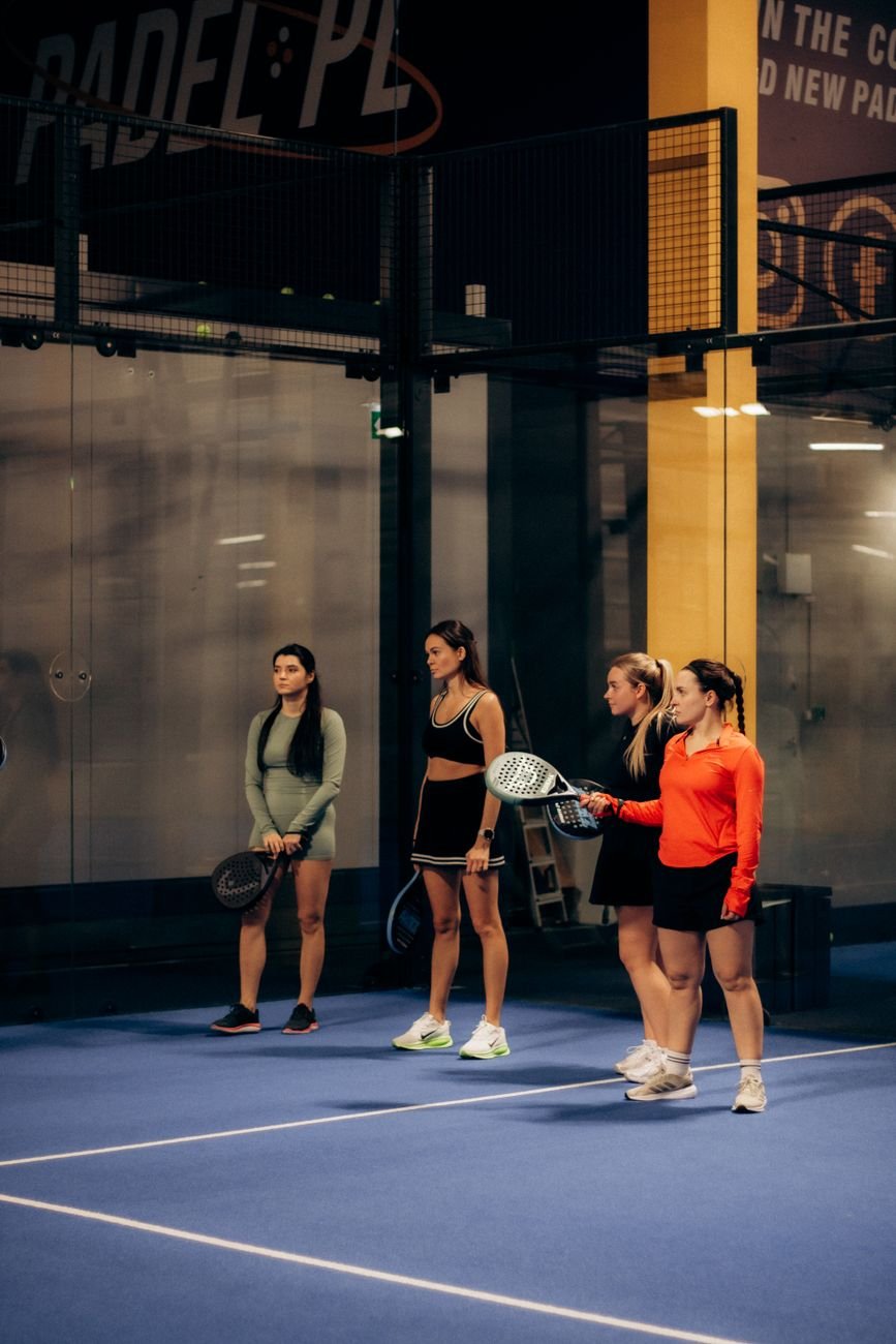 Quatre jugadores amb raquetes en una pista de pàdel coberta.